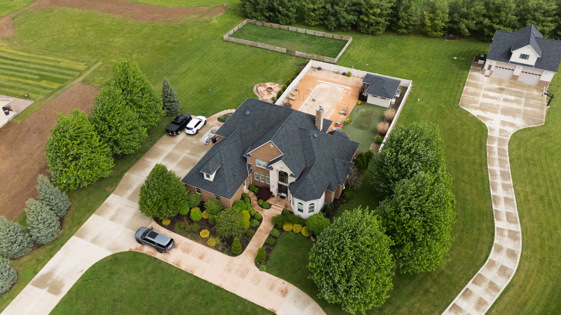 Oblique aerial showing the finished charcoal GAF roof against the brick-and-stone elevation — Whispering Pines, Bellefontaine, Ohio roof replacement by Peak One Restorations