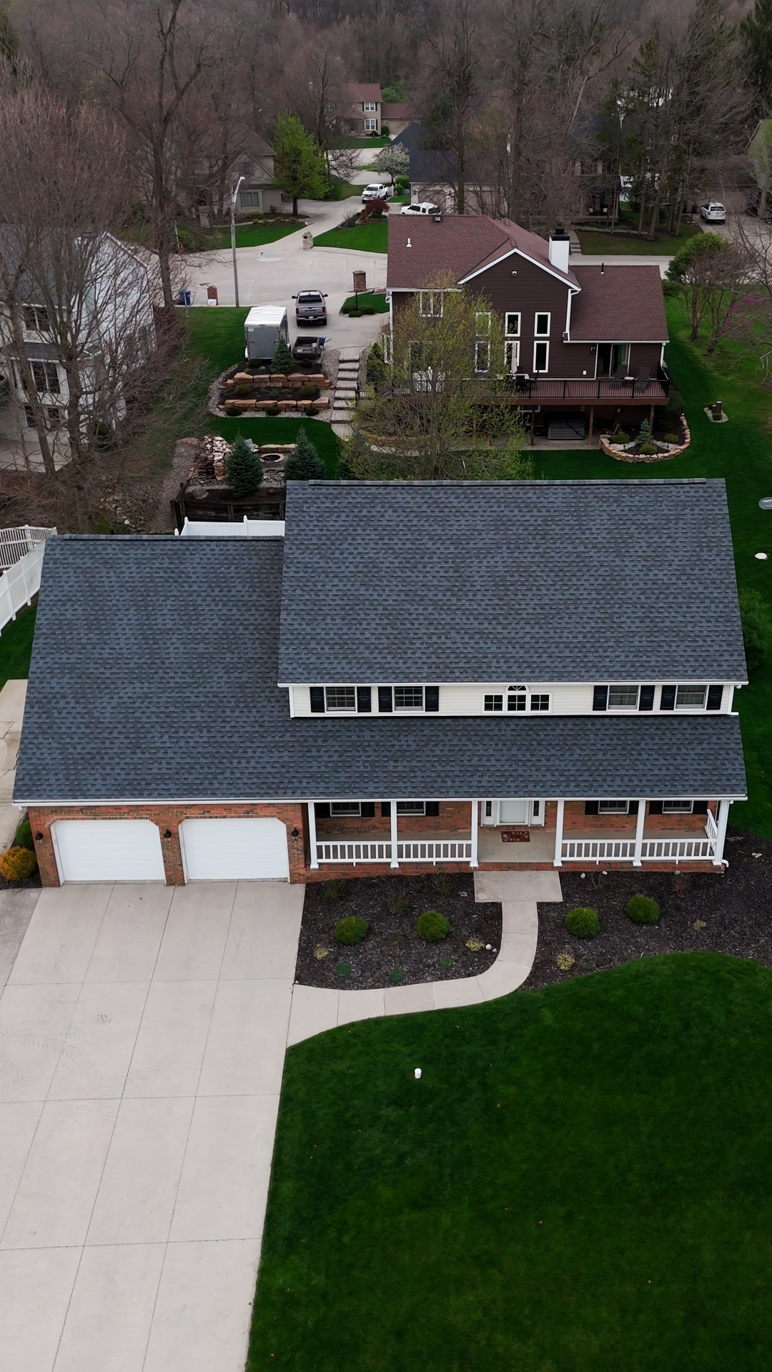 Oblique aerial showing the finished Pewter Gray GAF roof on the two-story brick colonial in its Whispering Pines context — Bellefontaine, Ohio referral roof replacement by Peak One Restorations