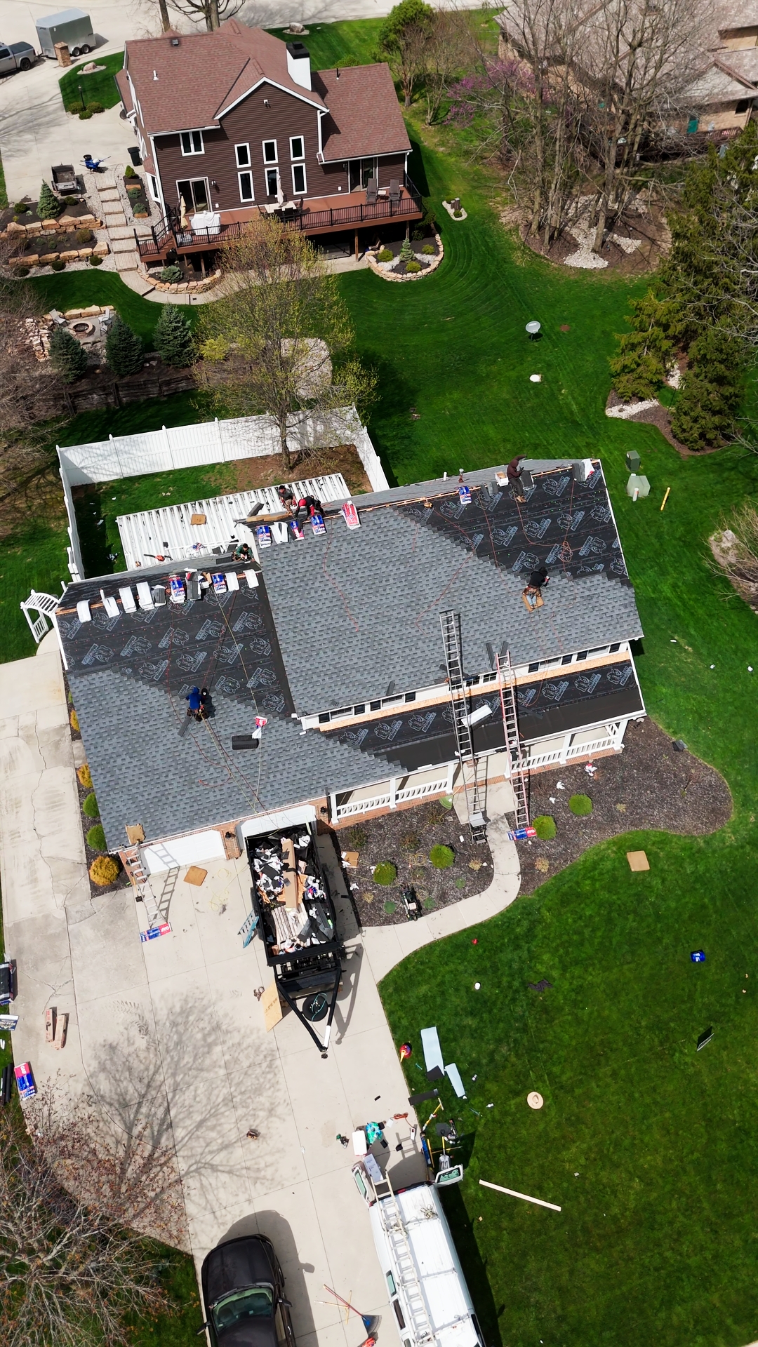 Mid-install aerial of the Peak One crew on the roof with synthetic underlayment dried-in and shingle bundles staged — Whispering Pines, Bellefontaine, Ohio